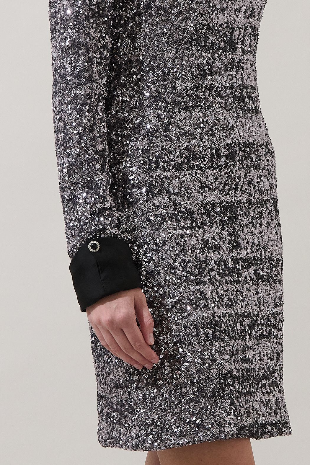 Close-up of silver sequins and a black contrast cuff with decorative button on the Sugarlips Alexa mini dress.