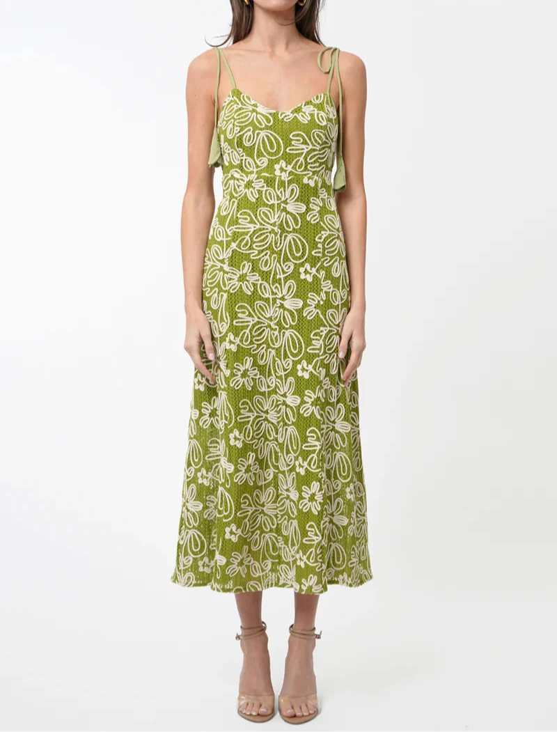 Woman wearing green embroidered floral midi dress with tie-shoulder straps and fitted bodice, styled for summer elegance.