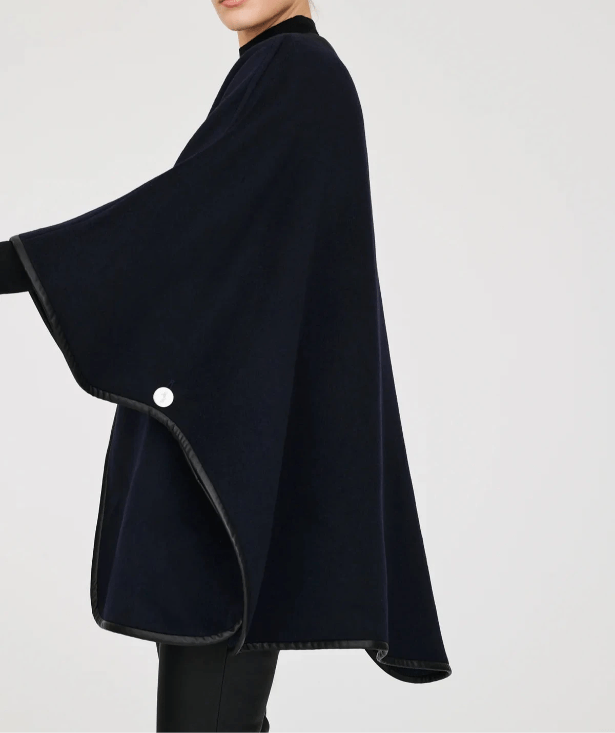 Side view of a model wearing the Weill Paris reversible wool cape in navy, highlighting the cape’s flowing poncho-style silhouette, black vegan leather trim, and elegant drape, creating a chic Parisian winter look