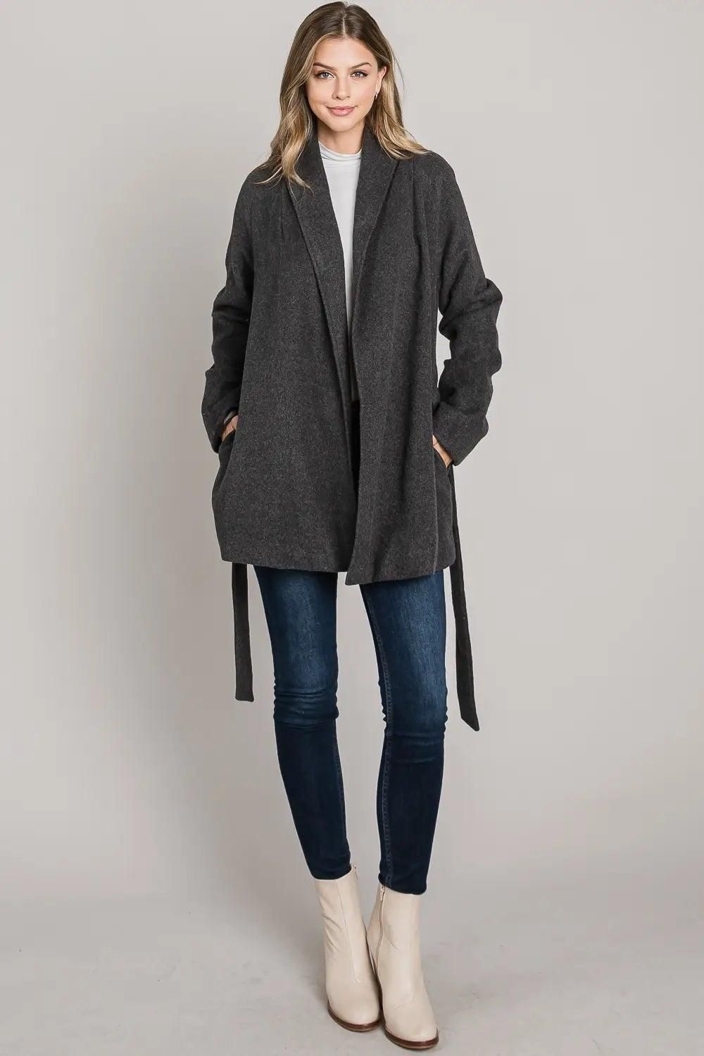 Full-length view of the charcoal collared wrap coat worn open over an outfit, highlighting the coat’s drape, lapel collar, and two side pockets.