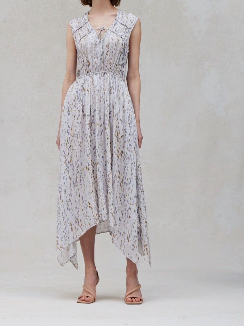 Sleeveless handkerchief‑hem midi dress in light ivory with blue‑dusk and taupe speckled print, split V‑neck with tie and softly cinched waist.