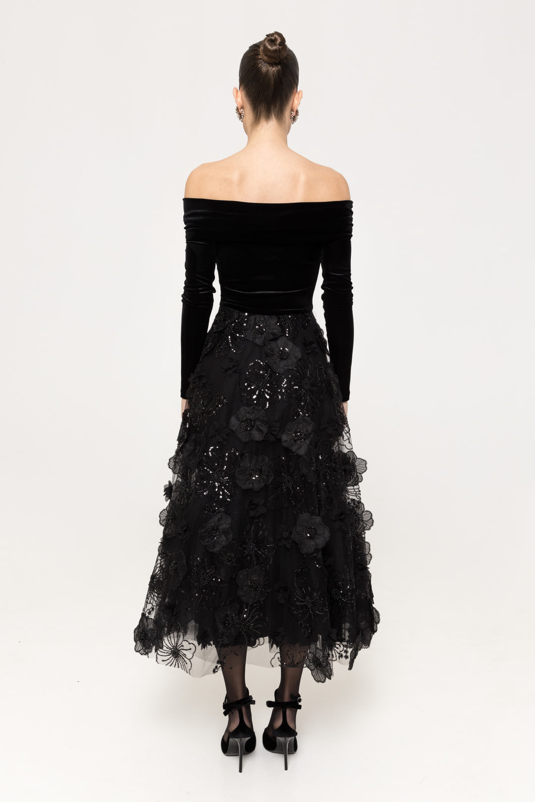 Back of black off‑shoulder velvet top with layered embellished tulle midi skirt.
