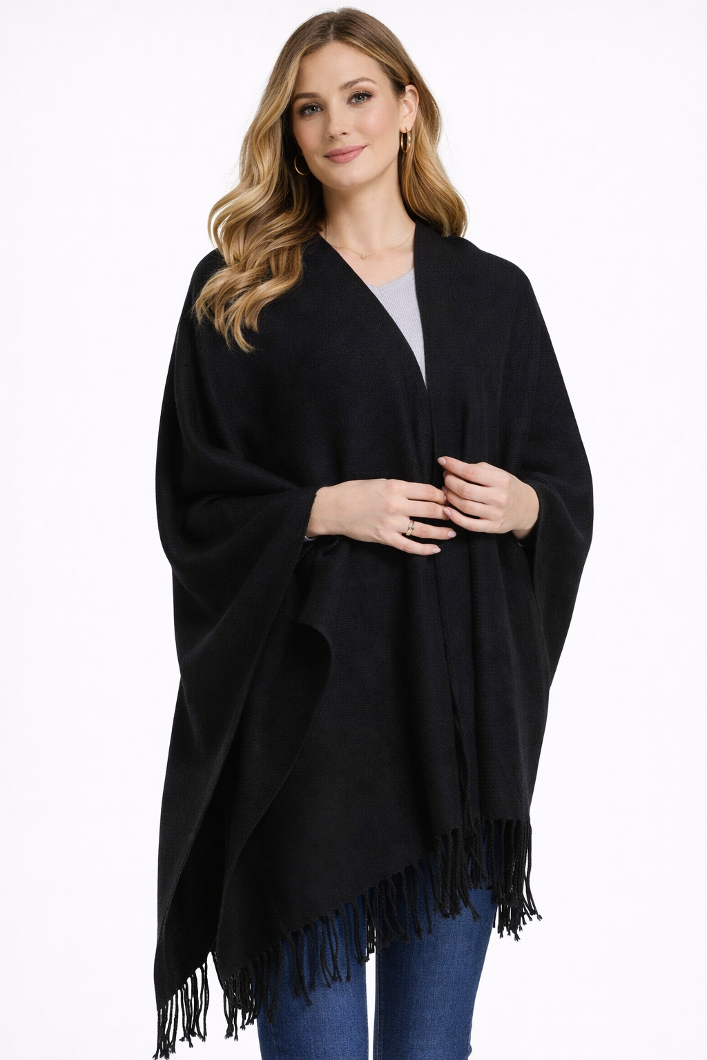 Front view of woman wearing a black poncho with fringe on a white background