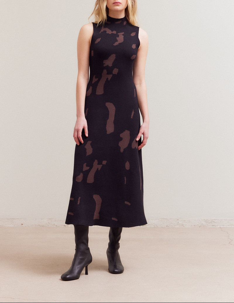 Woman wearing a black sleeveless dress with abstract pattern on a plain background