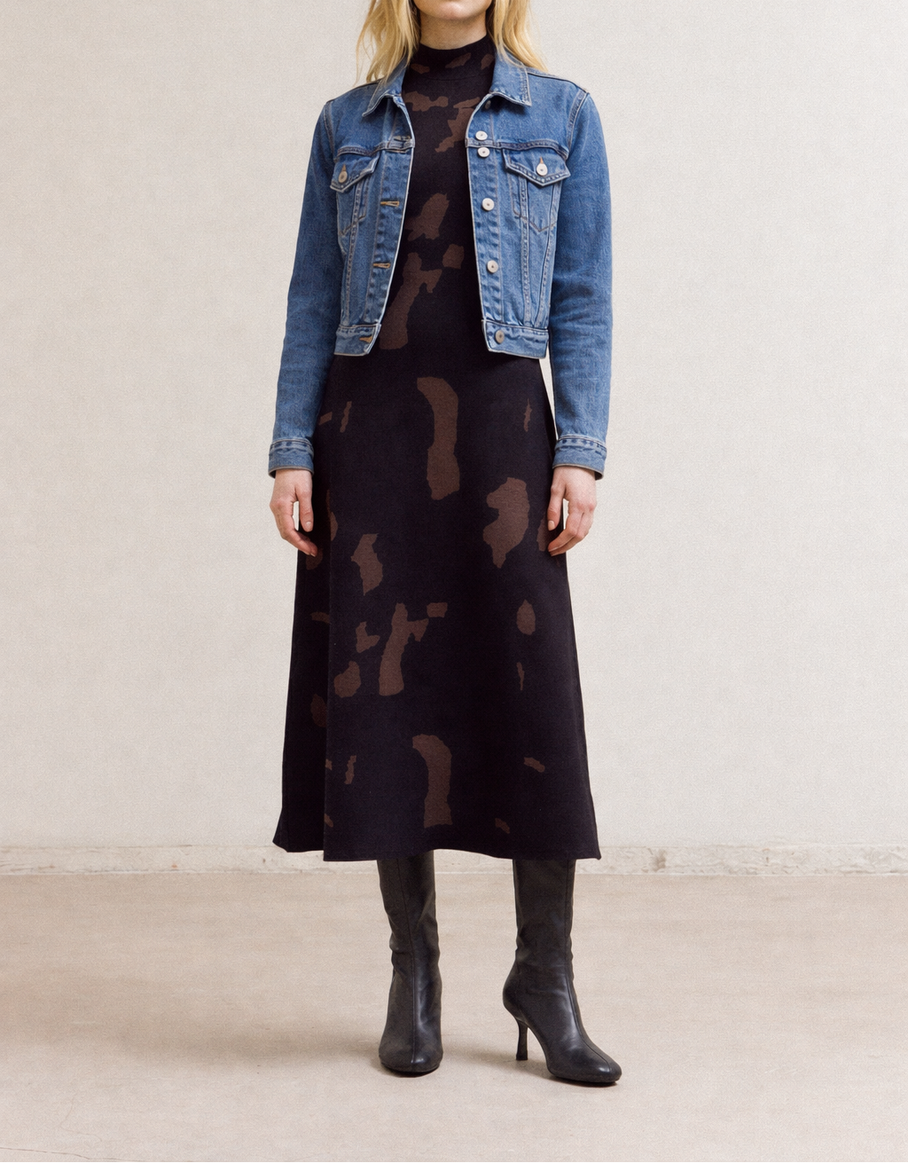 Woman wearing a denim jacket, black Fitted Knit maxi dress, and black boots on a plain background