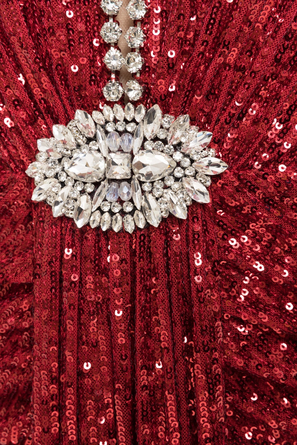 Close‑up detail of the red sequined fabric with a dazzling crystal‑embellished brooch and crystal chain trimming, showing the intricate beadwork and shimmering sequins.
