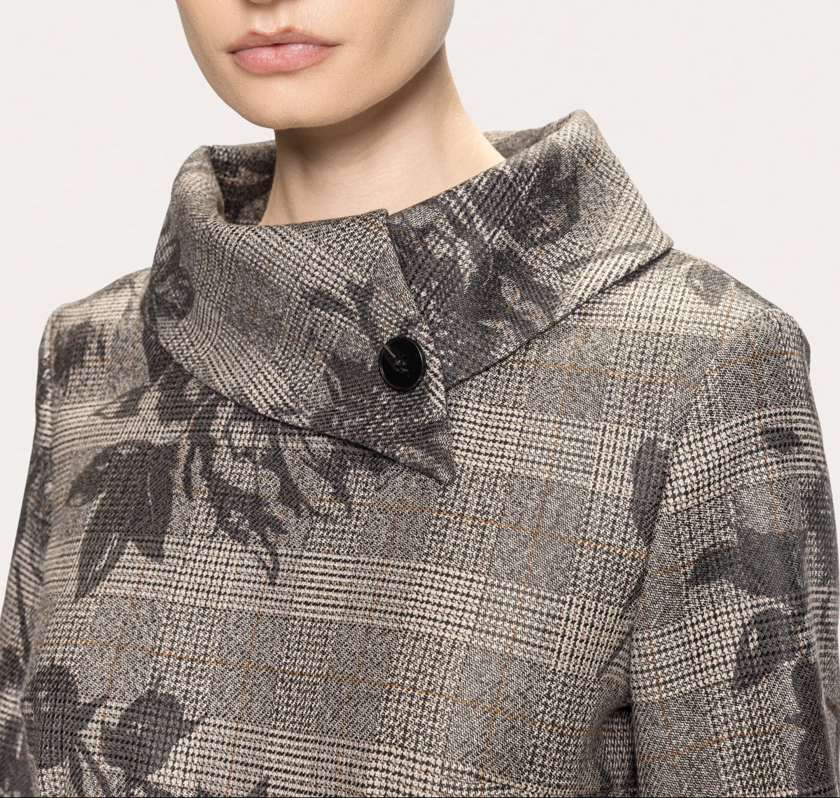 Close-up of the asymmetric high collar and black button on NISSA's gray floral plaid dress.