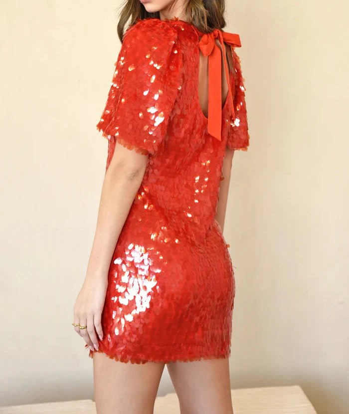 Back view of red paillette mini dress showing keyhole back with self‑tie bow and short sleeves