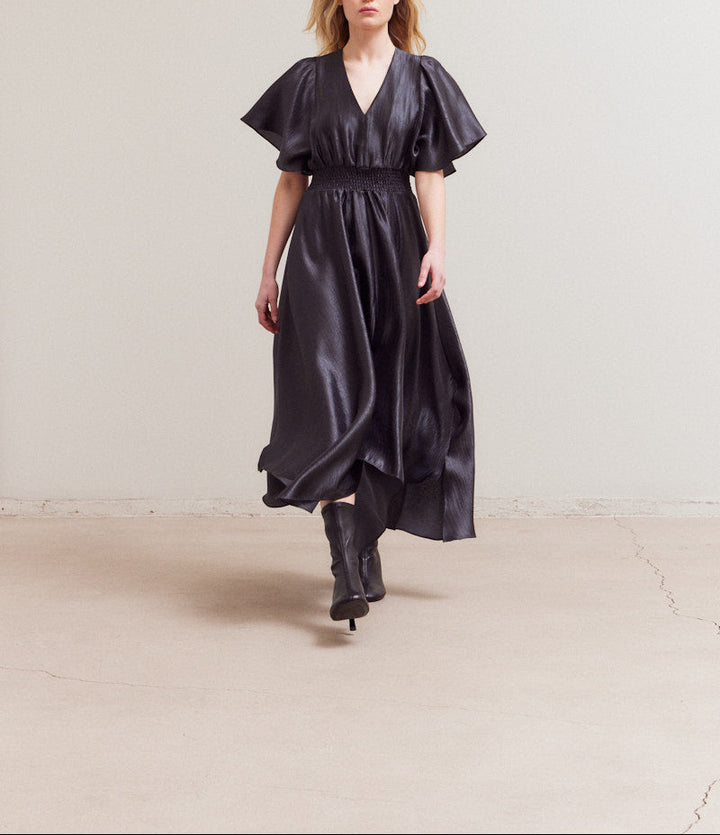 Mid-stride motion shot highlighting the elegant drape and asymmetry of the unbalanced maxi dress