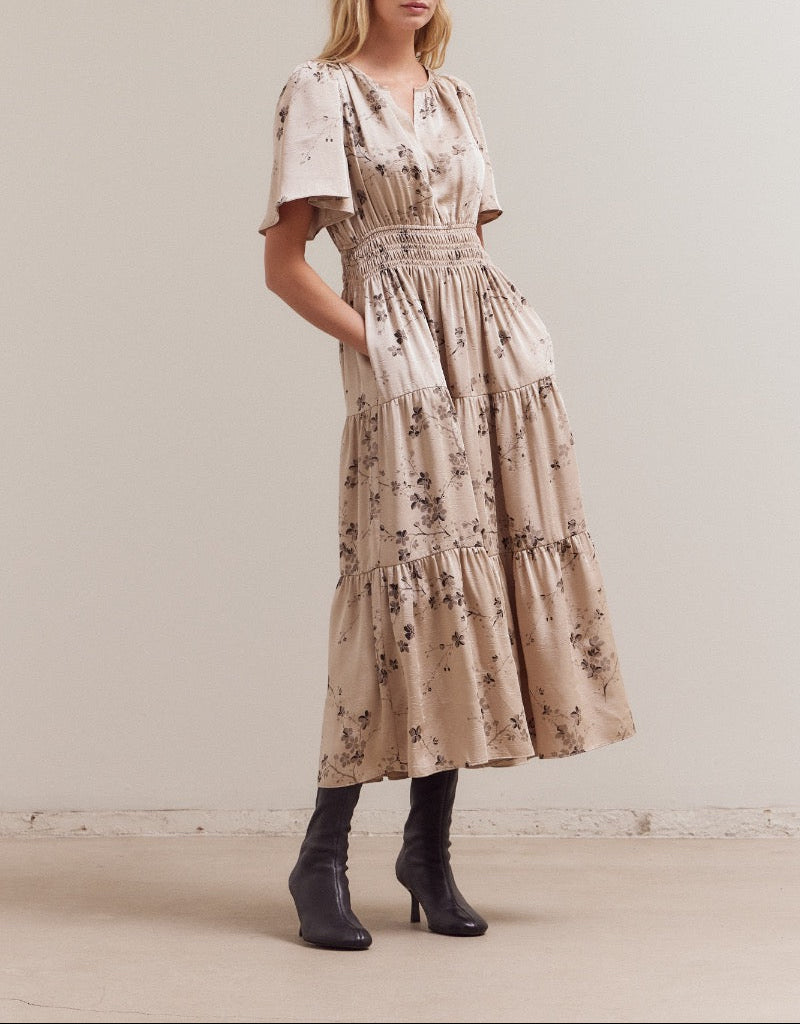 Front angled view showing the flowy tiered skirt and smocked waistband of the natural floral midi dress with pockets.