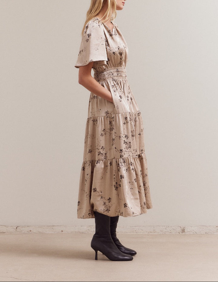 Left side profile of the natural floral dress showing flutter sleeve, pocket detail and boot‑friendly midi length.