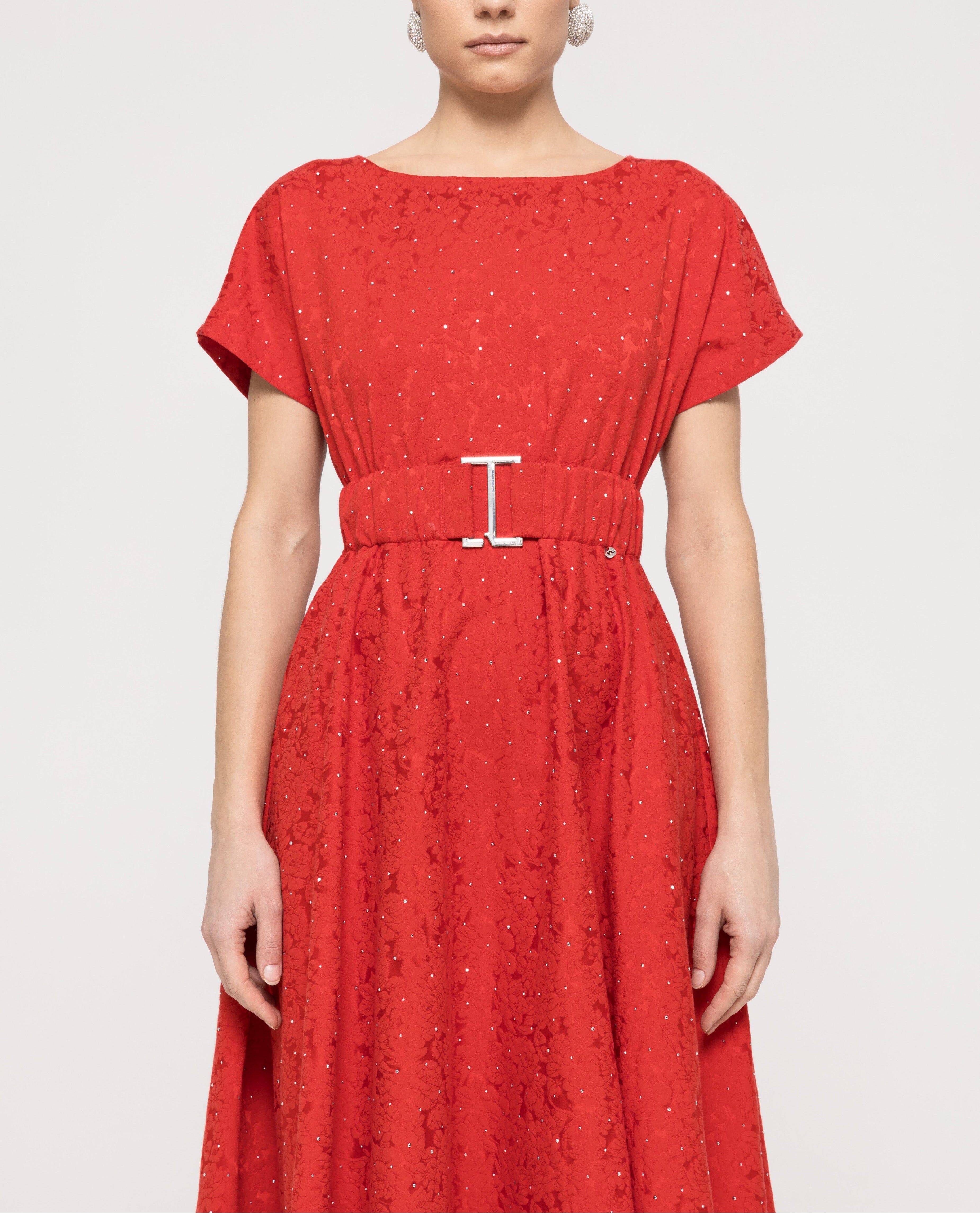 Bodice of red rhinestone‑embellished brocade dress showing boat neck, short sleeves and silver‑buckle belt.