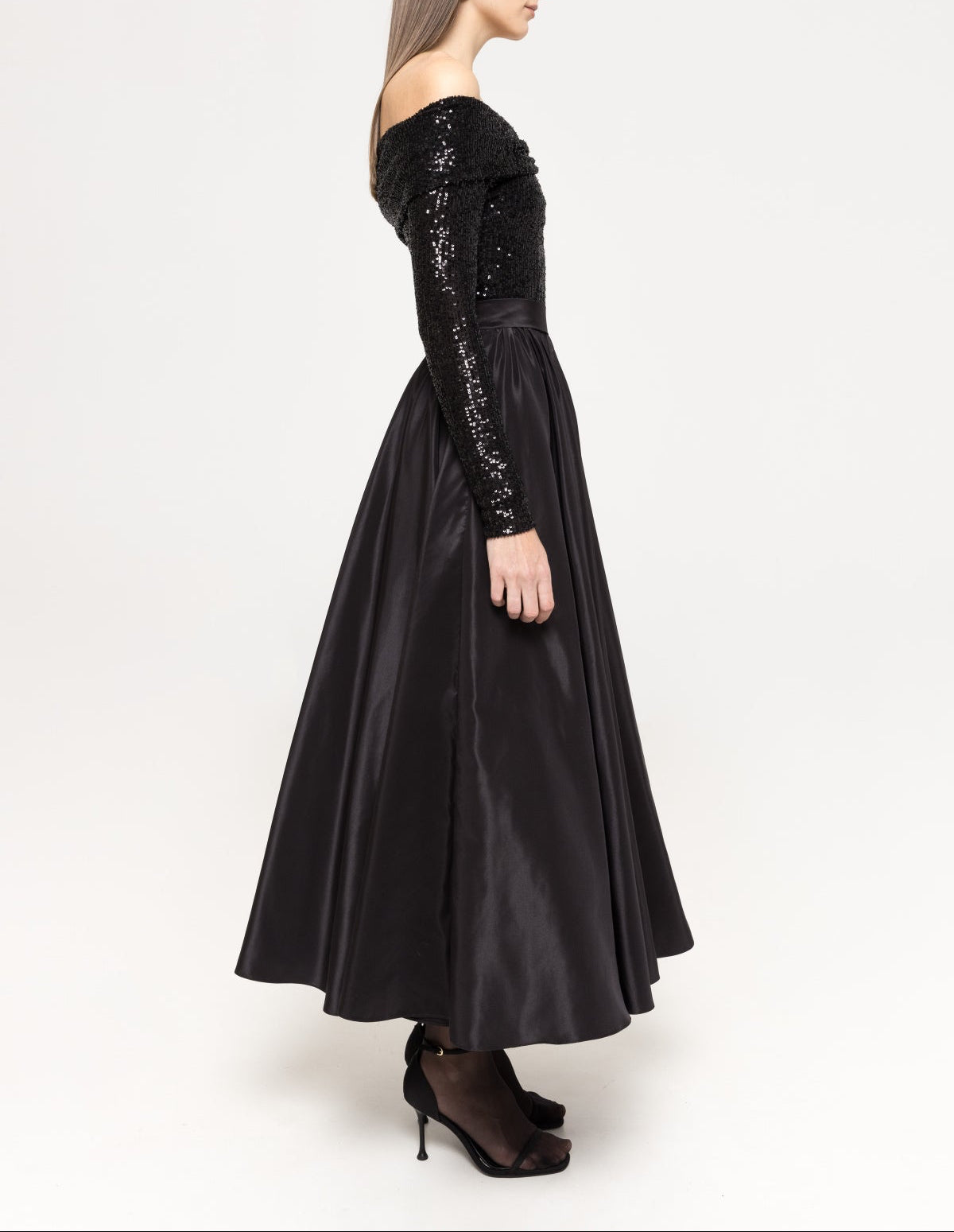 Side view showing the off‑the‑shoulder neckline, slim sequin sleeves, fitted waist and flowing taffeta A‑line midi skirt.