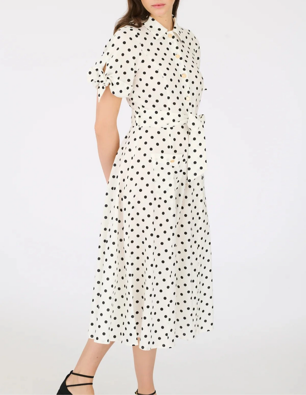 Model wearing white midi polka dot shirt dress with tie sleeves, button-down front, and waist belt