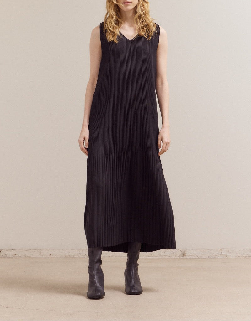 A model wearing a black sleeveless pleated V‑neck maxi dress with a relaxed, ankle‑length silhouette and fine vertical pleats.