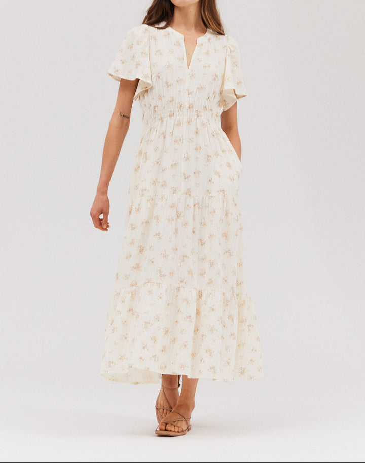 A woman wearing a mid-length printed gauze dress with short sleeves and a V-neckline, in a floral pattern, color beige.