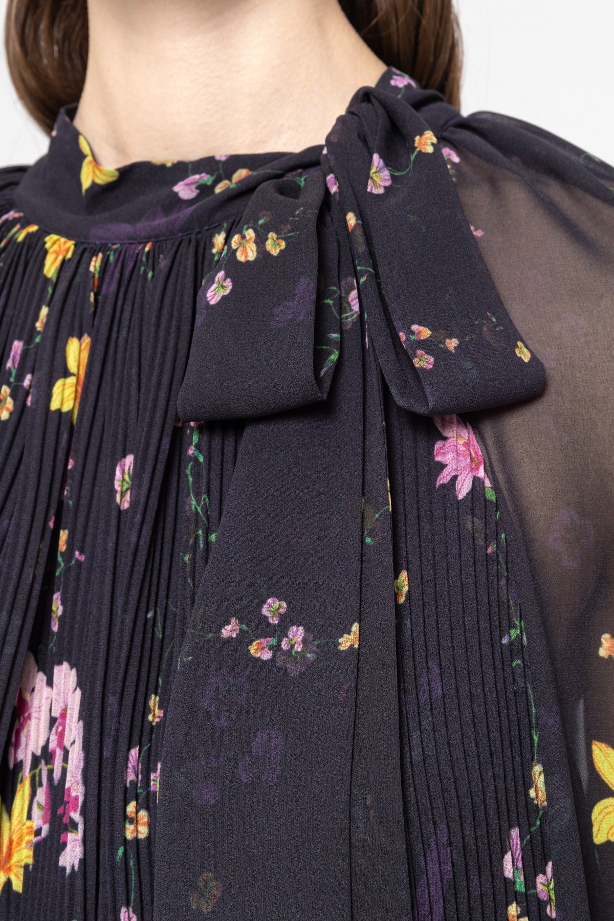 Close‑up of floral chiffon with fine pleats and scarf‑tie bow neckline on black dress