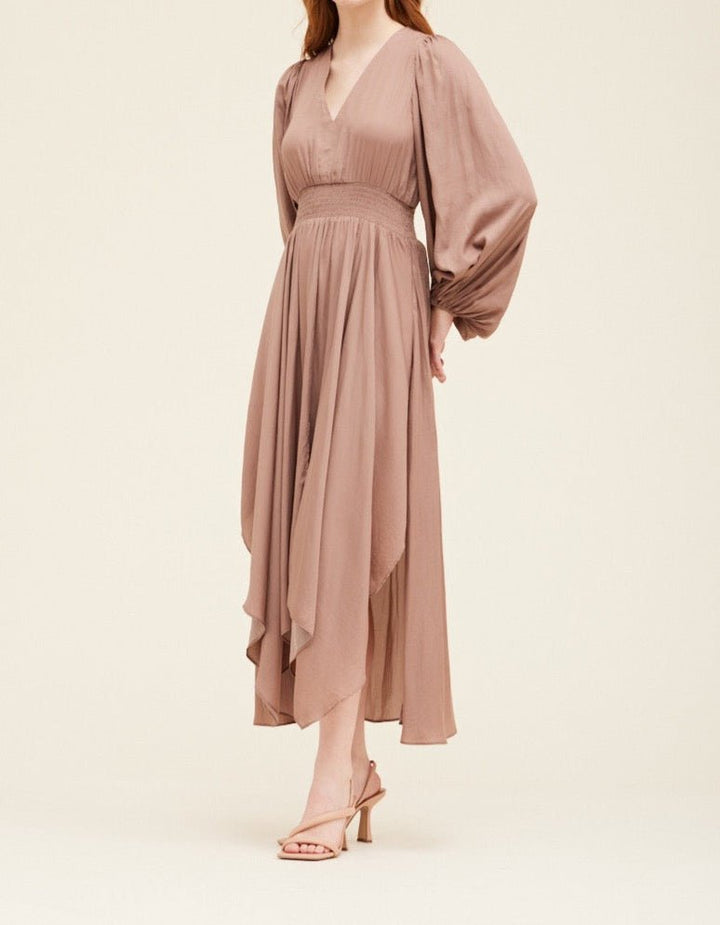 Side view of dusty orchid satin maxi dress highlighting the flowy skirt, smocked waistband, and sheer long sleeves.
