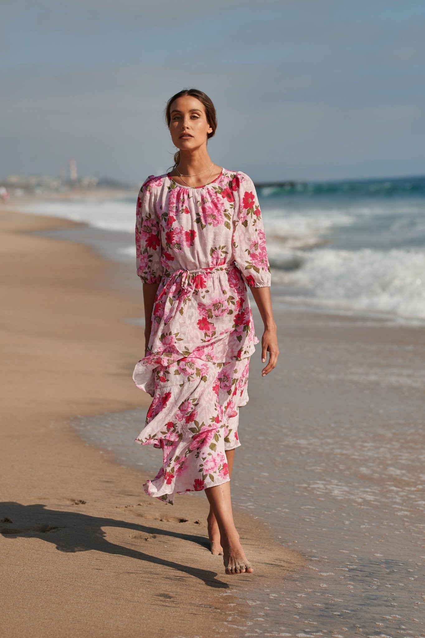 Pink floral asymmetrical ruffle midi dress with 3/4 sleeves and tie waist in beach setting