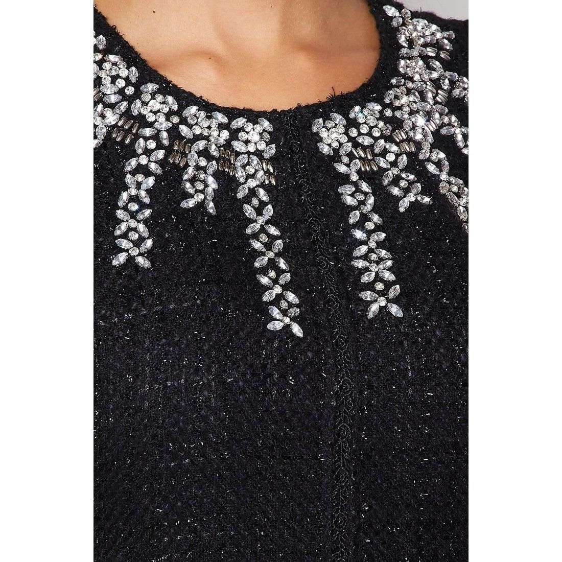 Close-up of clear faceted jewels and silver-tone bead details cascading around the dress’s round neckline against textured black fabric.