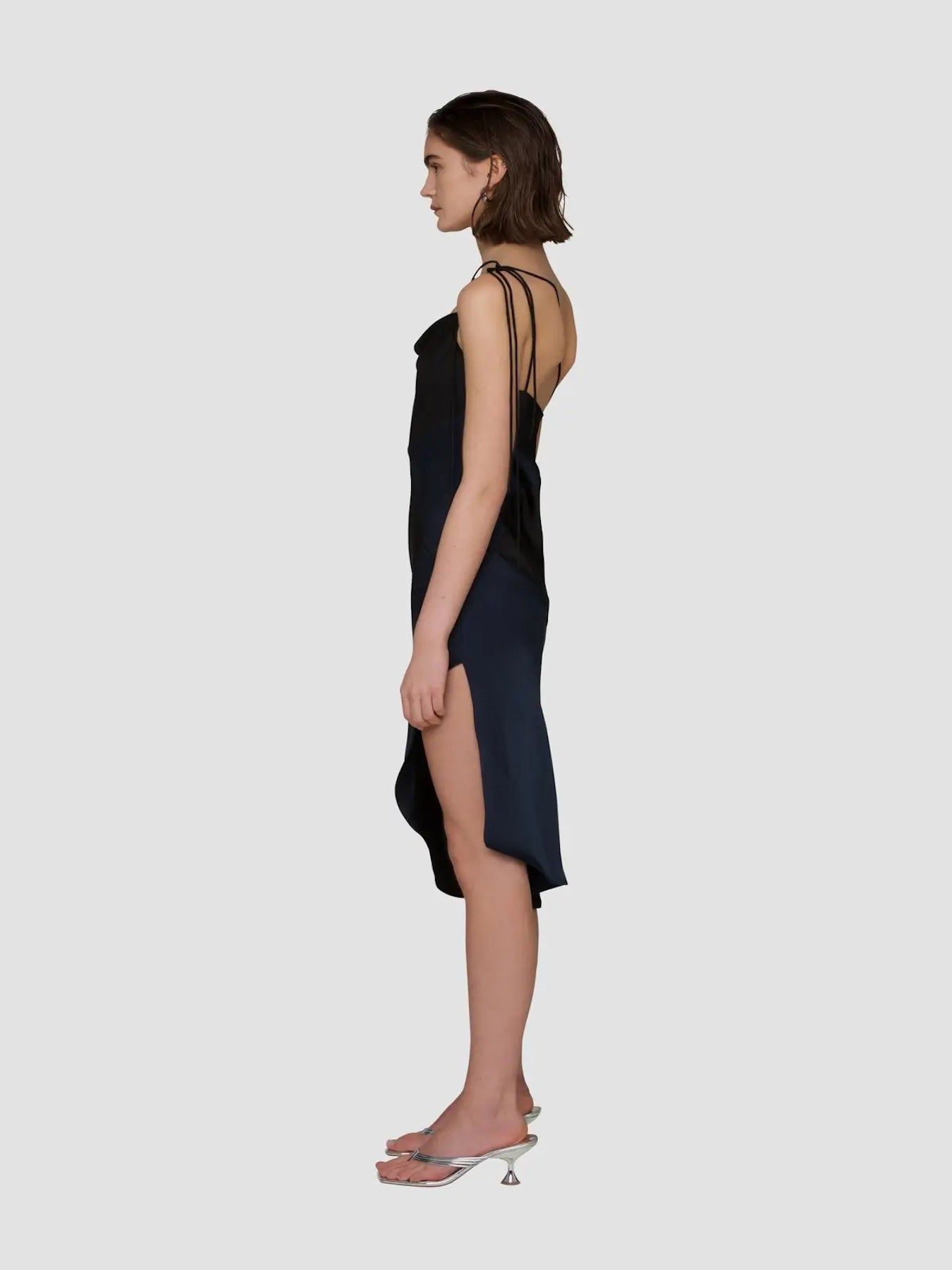 Side view of black and navy asymmetric satin midi dress with slit and slip silhouette