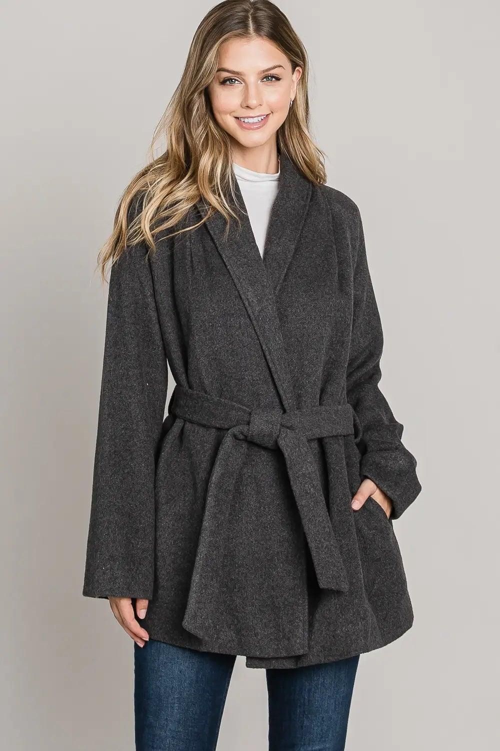 Front view of a woman wearing the charcoal gray Allie Rose collared pocket wrap coat, shown with the belt tied at the waist and hands in pockets.