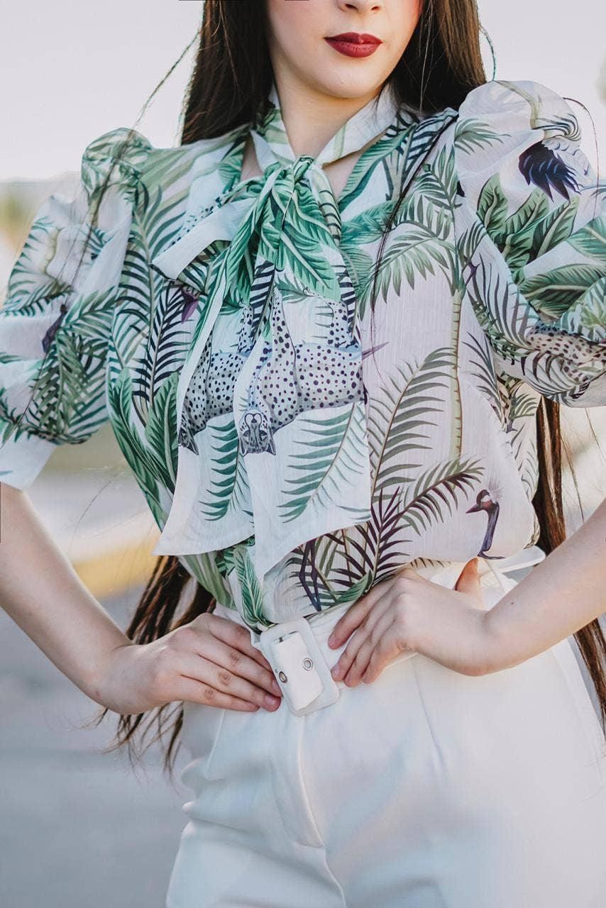 Close-up of the blouse’s tie neckline, green leaves, birds and spotted-cat motifs on a pale background.